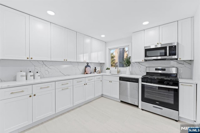 kitchen with sink, backsplash, white cabinets, and appliances with stainless steel finishes