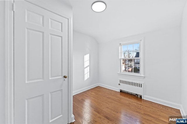 empty room with wood-type flooring, lofted ceiling, and radiator heating unit