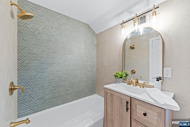 bathroom featuring vanity, vaulted ceiling, tile walls, and tiled shower / bath