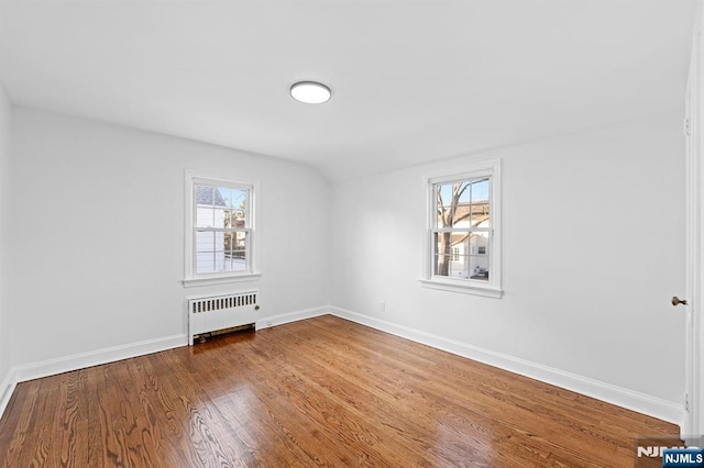 empty room with wood-type flooring, a healthy amount of sunlight, and radiator heating unit