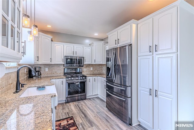 kitchen with light hardwood / wood-style flooring, appliances with stainless steel finishes, white cabinetry, hanging light fixtures, and light stone countertops