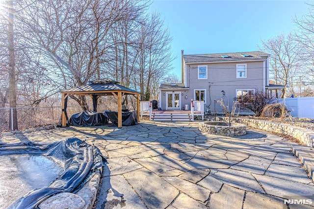 back of property with a fire pit, a wooden deck, a gazebo, a patio area, and french doors