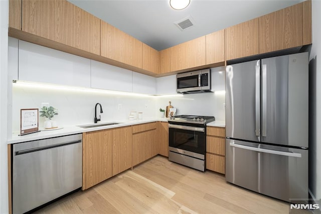 kitchen with stainless steel appliances, light brown cabinetry, light hardwood / wood-style floors, and sink