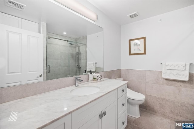 bathroom with tile walls, vanity, a shower with shower door, tile patterned floors, and toilet