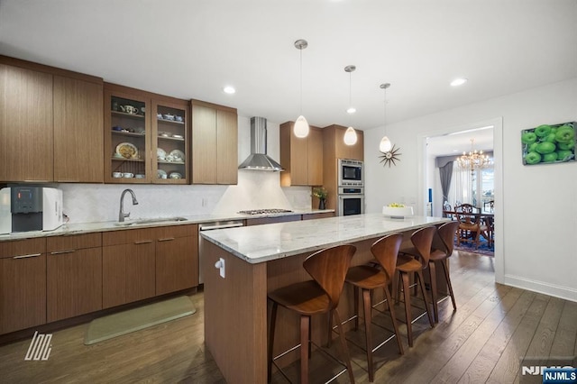 kitchen featuring sink, dark hardwood / wood-style floors, a kitchen island, stainless steel appliances, and wall chimney range hood