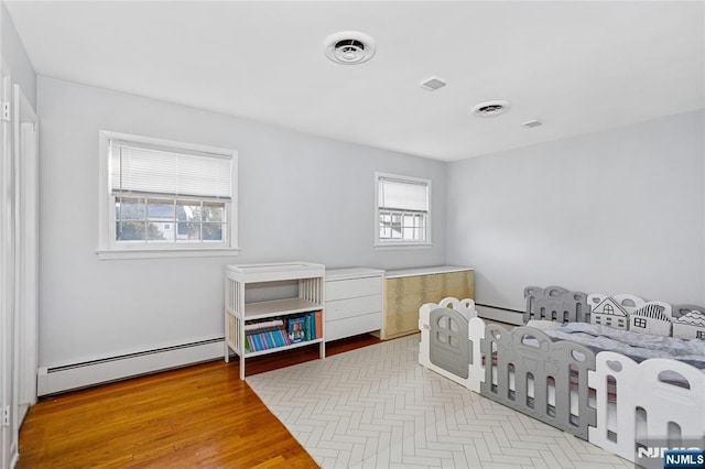 bedroom with a baseboard heating unit and light hardwood / wood-style floors