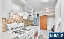 kitchen featuring white range with gas cooktop, backsplash, white cabinetry, and sink