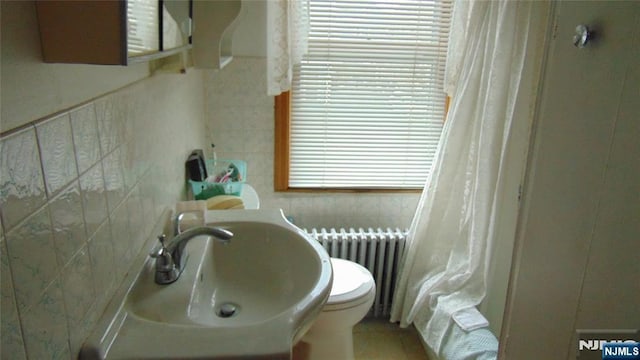 bathroom featuring radiator heating unit, toilet, sink, and tile walls