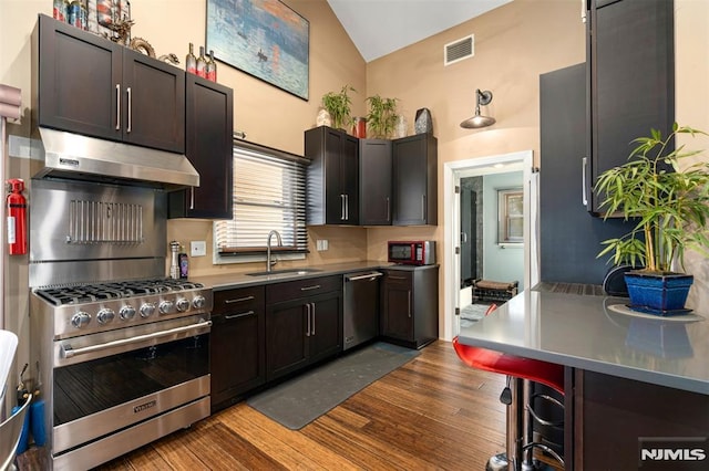 kitchen featuring dark brown cabinetry, a kitchen bar, sink, stainless steel appliances, and hardwood / wood-style floors