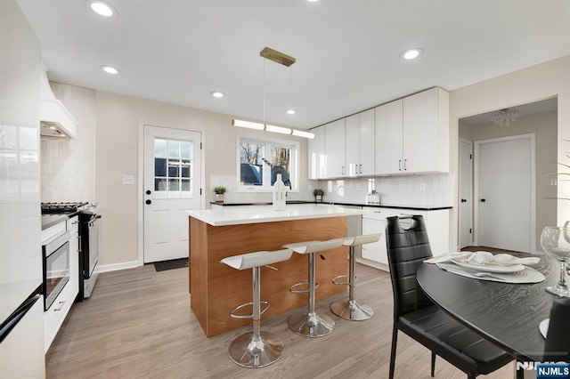 kitchen featuring a kitchen island, white cabinets, hanging light fixtures, gas range, and light hardwood / wood-style flooring