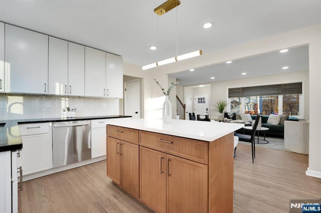 kitchen featuring stainless steel dishwasher, white cabinets, light hardwood / wood-style floors, and decorative light fixtures