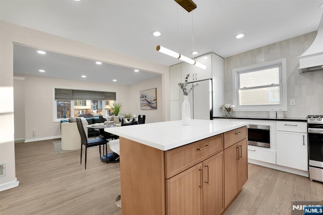 kitchen with stainless steel range oven, refrigerator, hanging light fixtures, custom range hood, and light hardwood / wood-style floors