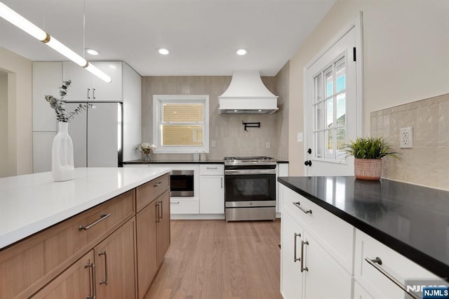 kitchen featuring stainless steel gas stove, tasteful backsplash, white cabinetry, custom exhaust hood, and light wood-type flooring