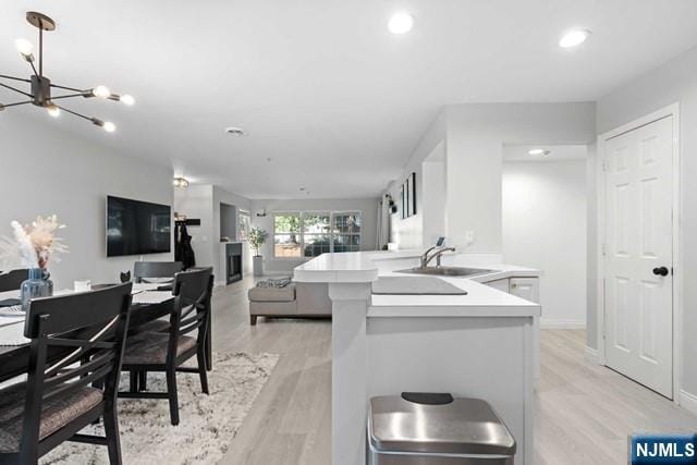 kitchen featuring sink, white cabinetry, light hardwood / wood-style floors, a center island with sink, and a chandelier