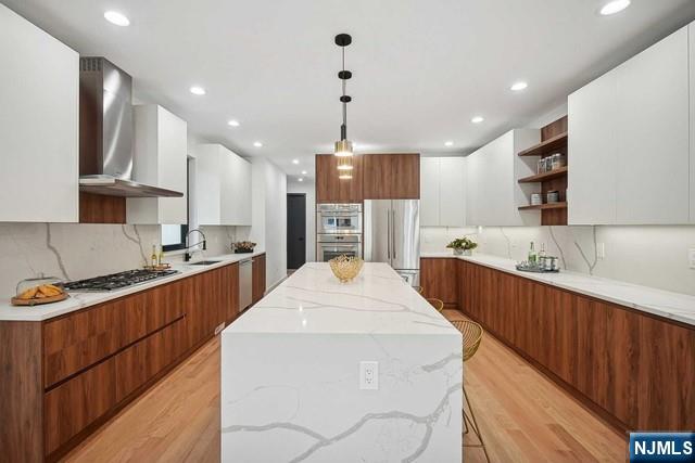 kitchen featuring white cabinetry, stainless steel appliances, a center island, and wall chimney exhaust hood