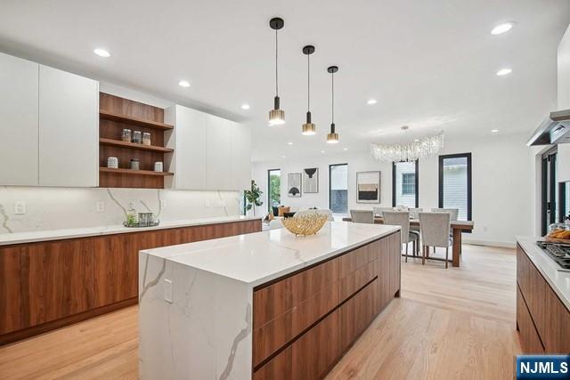 kitchen featuring light hardwood / wood-style flooring, a kitchen island, white cabinets, pendant lighting, and backsplash