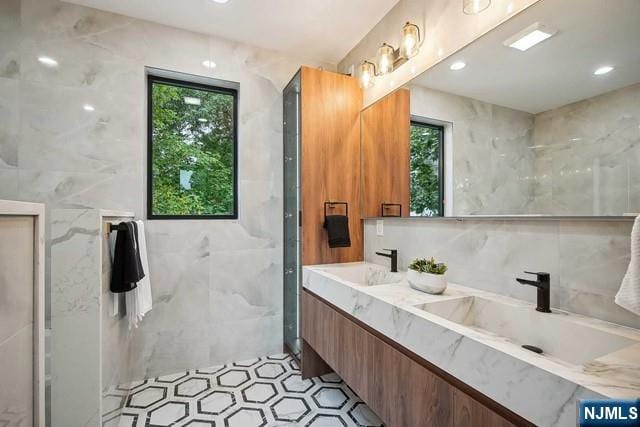 bathroom with walk in shower, vanity, and tile walls