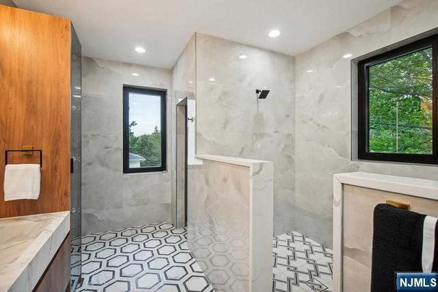 bathroom featuring plenty of natural light, tile walls, vanity, and a tile shower