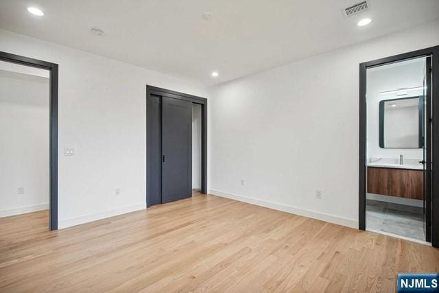 unfurnished bedroom featuring multiple closets, light wood-type flooring, and ensuite bath