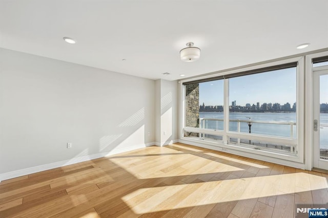 spare room with a water view, a wall of windows, and light wood-type flooring