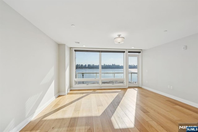 empty room featuring light wood-type flooring, expansive windows, and a water view