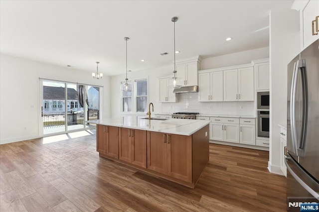 kitchen with light stone countertops, an island with sink, appliances with stainless steel finishes, and white cabinets