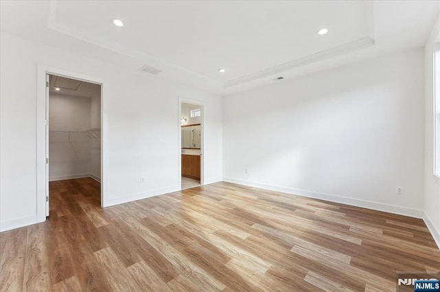 unfurnished bedroom with a tray ceiling, light hardwood / wood-style floors, and a spacious closet