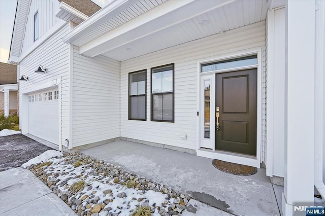 snow covered property entrance featuring a porch and a garage