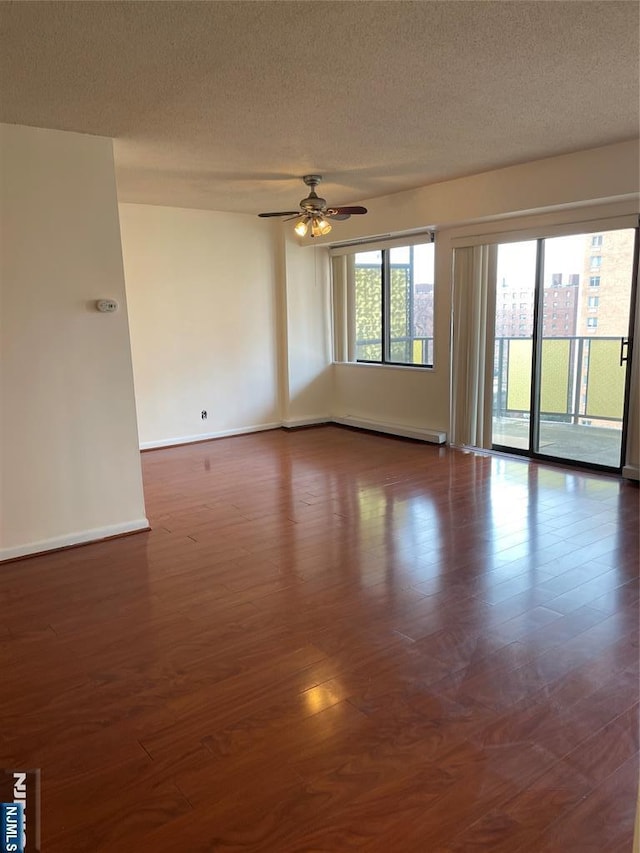 spare room featuring dark wood-type flooring, ceiling fan, baseboard heating, and a textured ceiling