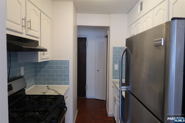 kitchen featuring stainless steel gas range, tasteful backsplash, refrigerator, dark tile patterned flooring, and white cabinets