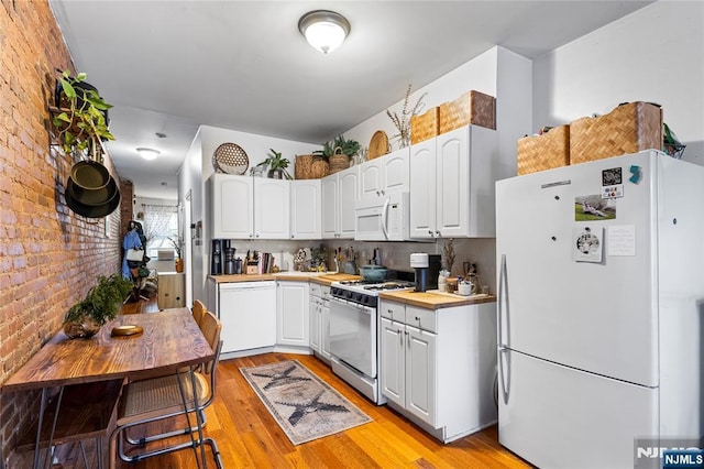 kitchen featuring white appliances, brick wall, and white cabinets