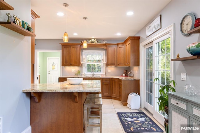 kitchen featuring pendant lighting, a kitchen breakfast bar, light tile patterned floors, light stone counters, and kitchen peninsula