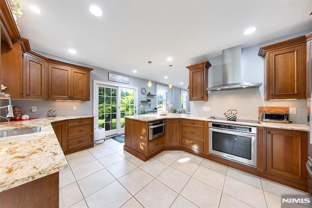 kitchen featuring wall chimney range hood, sink, hanging light fixtures, kitchen peninsula, and stainless steel oven