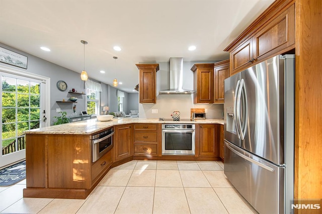 kitchen featuring appliances with stainless steel finishes, decorative light fixtures, light stone counters, kitchen peninsula, and wall chimney exhaust hood