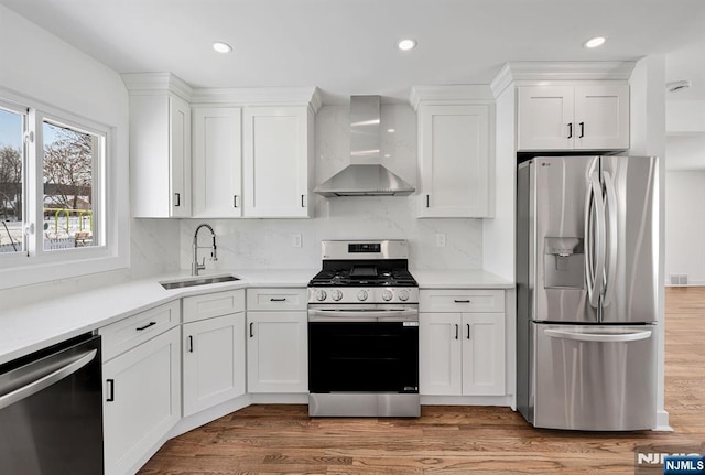 kitchen with wall chimney exhaust hood, appliances with stainless steel finishes, sink, and white cabinets