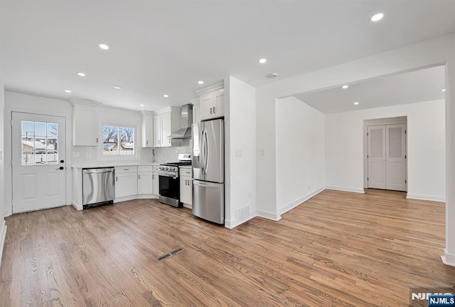 kitchen with light hardwood / wood-style floors, wall chimney exhaust hood, white cabinets, and appliances with stainless steel finishes