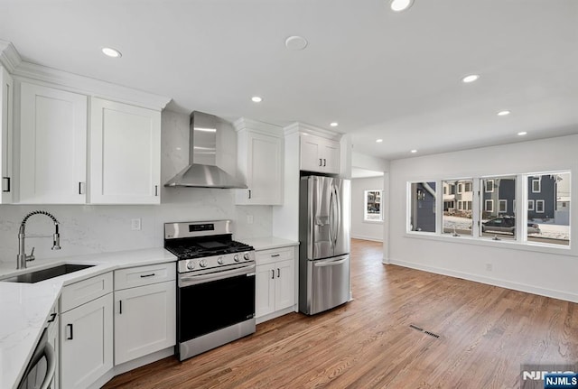 kitchen featuring sink, white cabinetry, light wood-type flooring, appliances with stainless steel finishes, and wall chimney range hood