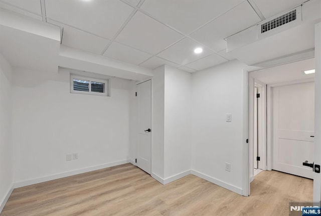 basement featuring a paneled ceiling and light wood-type flooring