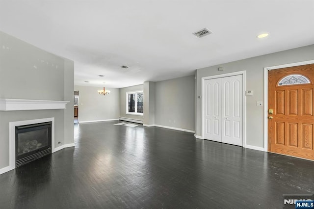 unfurnished living room with a chandelier, dark wood-type flooring, visible vents, baseboards, and a glass covered fireplace