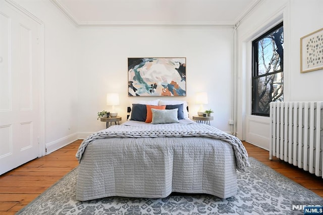 bedroom with ornamental molding, radiator heating unit, and wood-type flooring