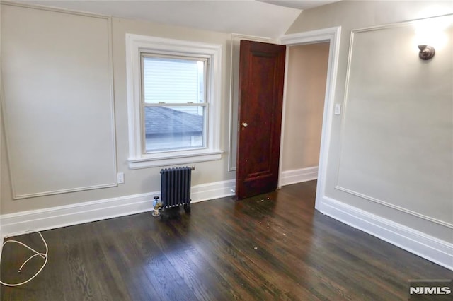 spare room with vaulted ceiling, dark wood-type flooring, and radiator heating unit