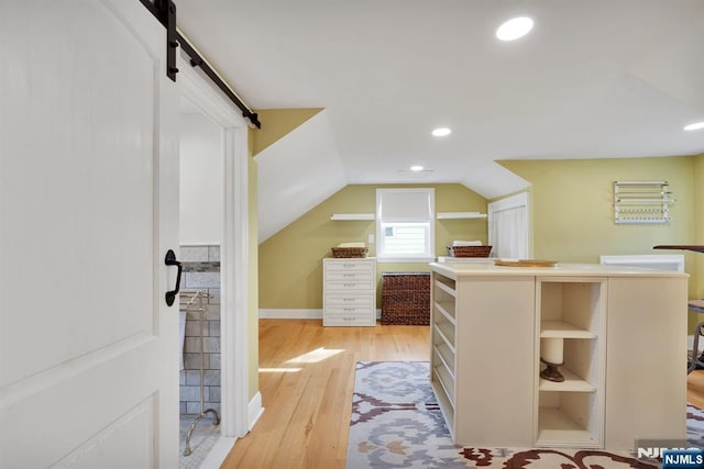 spacious closet with a barn door, vaulted ceiling, and light hardwood / wood-style flooring