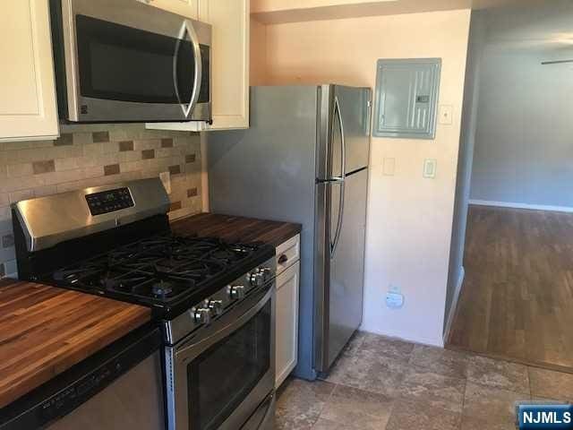 kitchen with wood counters, white cabinetry, electric panel, stainless steel appliances, and decorative backsplash