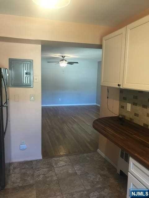 kitchen with black refrigerator, radiator heating unit, white cabinetry, backsplash, and ceiling fan