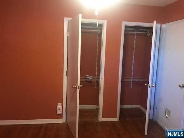 unfurnished bedroom featuring multiple closets and dark wood-type flooring