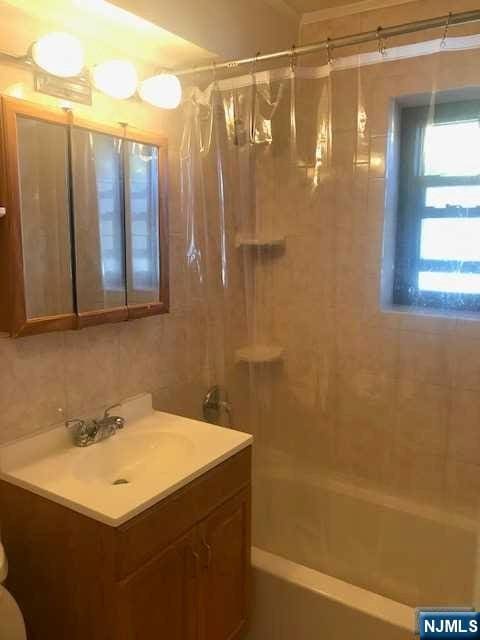 bathroom with tasteful backsplash, sink, tile walls, and shower / bath combination with curtain