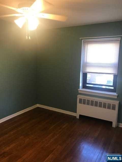 spare room featuring ceiling fan, radiator heating unit, and dark hardwood / wood-style floors