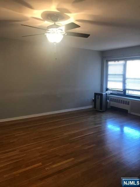 empty room featuring dark hardwood / wood-style flooring, radiator heating unit, and ceiling fan