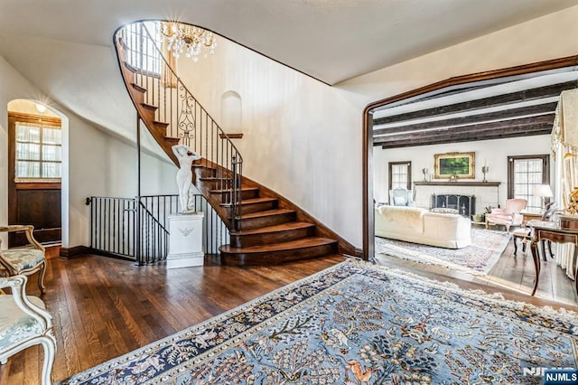 staircase featuring hardwood / wood-style flooring, an inviting chandelier, a wealth of natural light, and beam ceiling