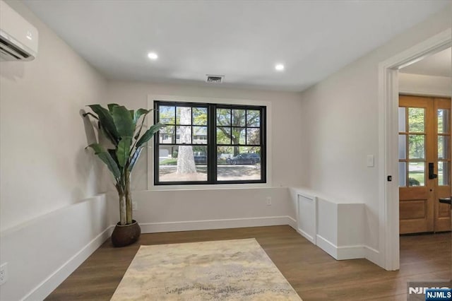 empty room featuring a wall mounted AC, wood finished floors, recessed lighting, and baseboards